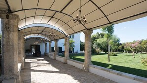An outdoor covered walkway with stone flooring, columns, and a hanging chandelier. - Parco degli Aranci (Cutrofiano)