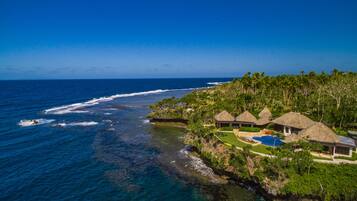 A coastal resort with thatched-roof villas, a swimming pool, and a view of the ocean.