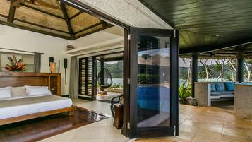 A spacious bedroom with a large bed, a glass door leading to a balcony with a pool, and a view of the mountains.