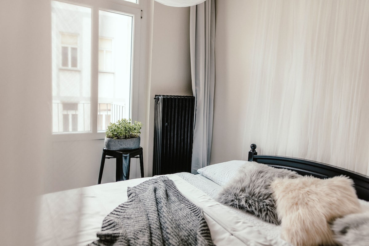 A bedroom with a bed, a potted plant, a radiator, and a window.