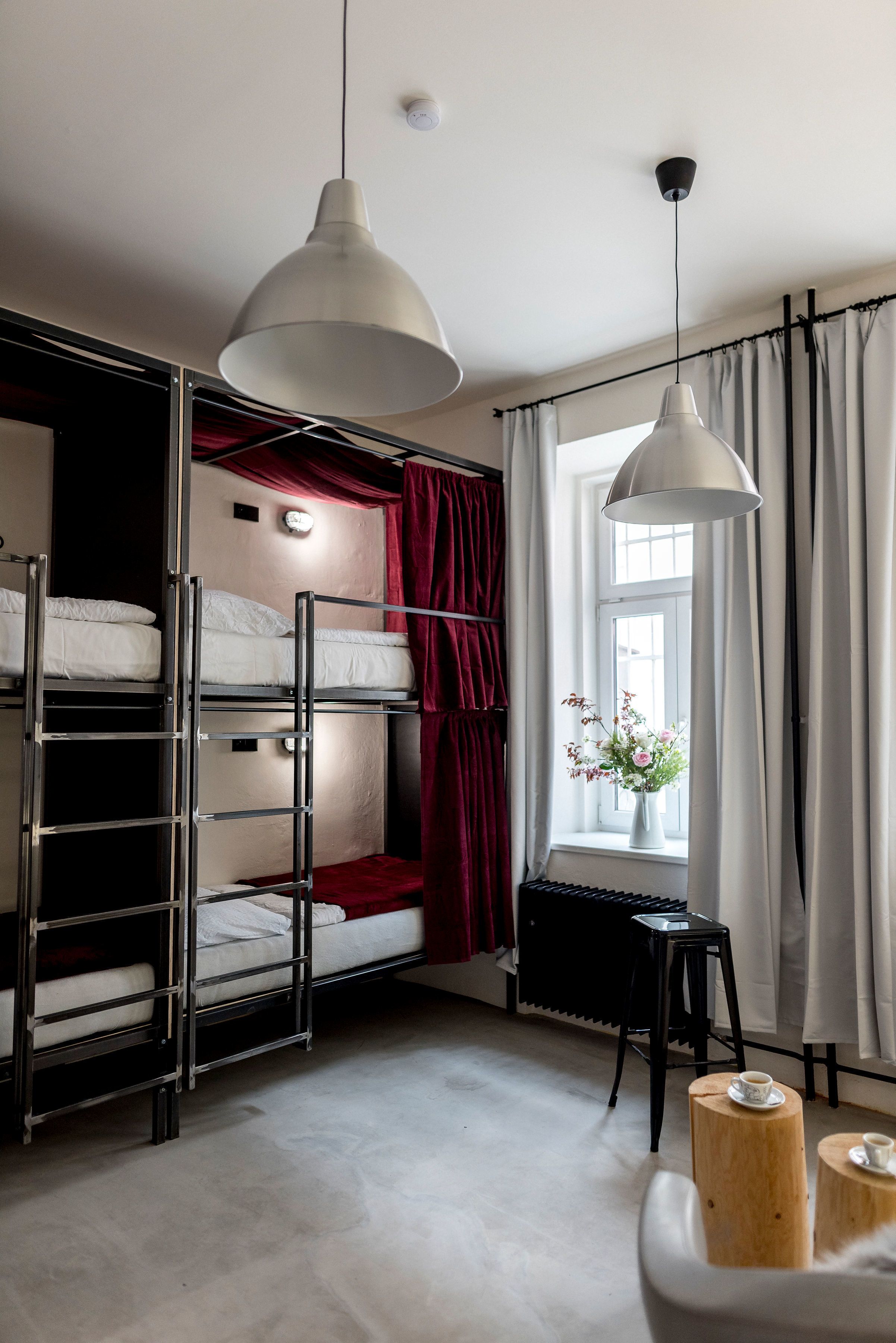 Dormitorio con literas, ventana, cortinas, una mesita con una taza y una lámpara colgante.