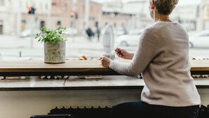 A person sitting at a table with a potted plant and a cup, overlooking a street with cars and buildings. - Wake Up Wellness Hostel by goodnite cz (Brno)
