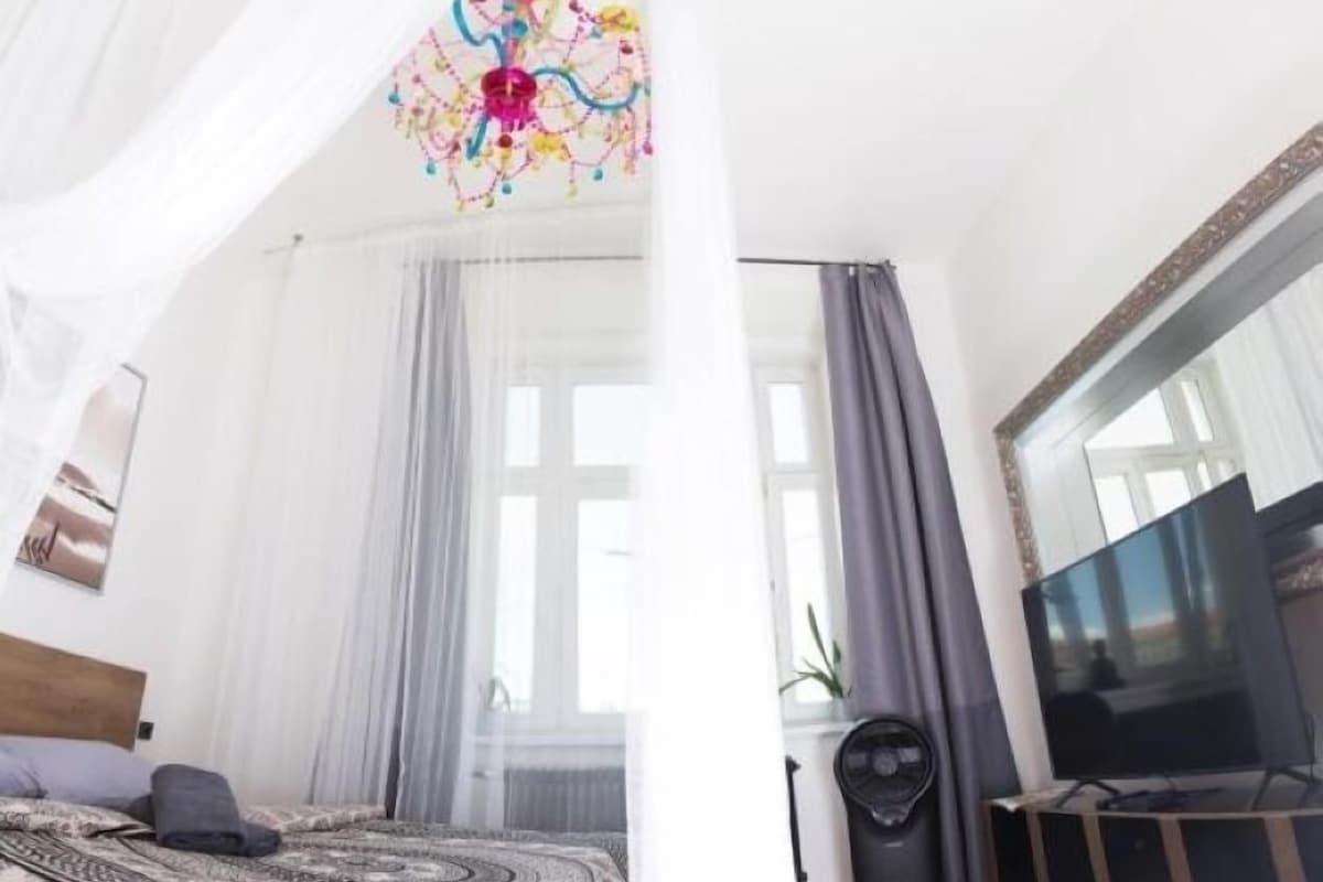 A bedroom with a bed, curtains, a TV, and a ceiling light fixture.