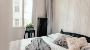 A bedroom with a bed, a potted plant, a radiator, and a window with curtains. - Wake Up Wellness Hostel by goodnite cz (Brno)