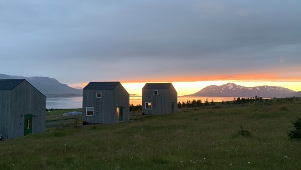 Three wooden cabins in a grassy field with a mountain and sunset in the background. - Sunnuhlid houses (Akureyri)