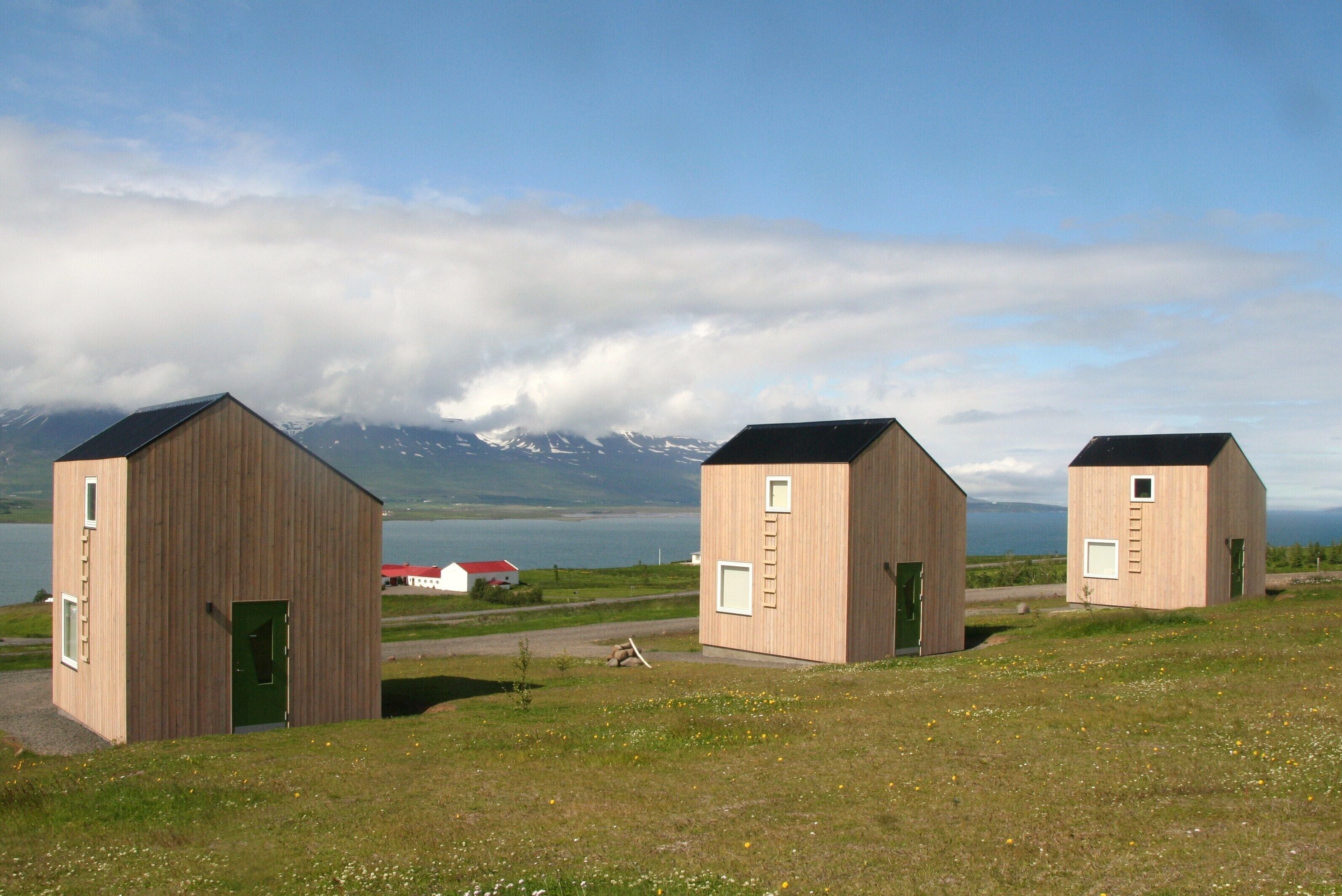 Tres cabañas de madera con montañas al fondo y un lago.