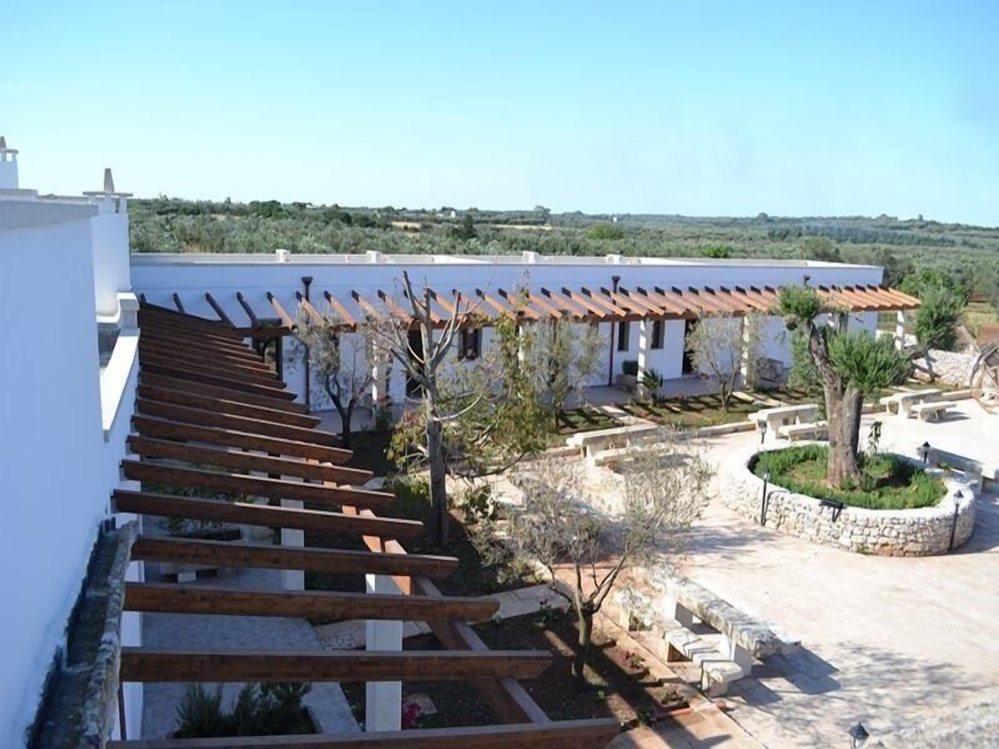 A white building with a wooden pergola and a stone pathway.
