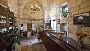 Une cuisine aux murs de pierre, dotée d’un plafond haut, d’un îlot central et d’un coin bar où sont exposés des fruits.