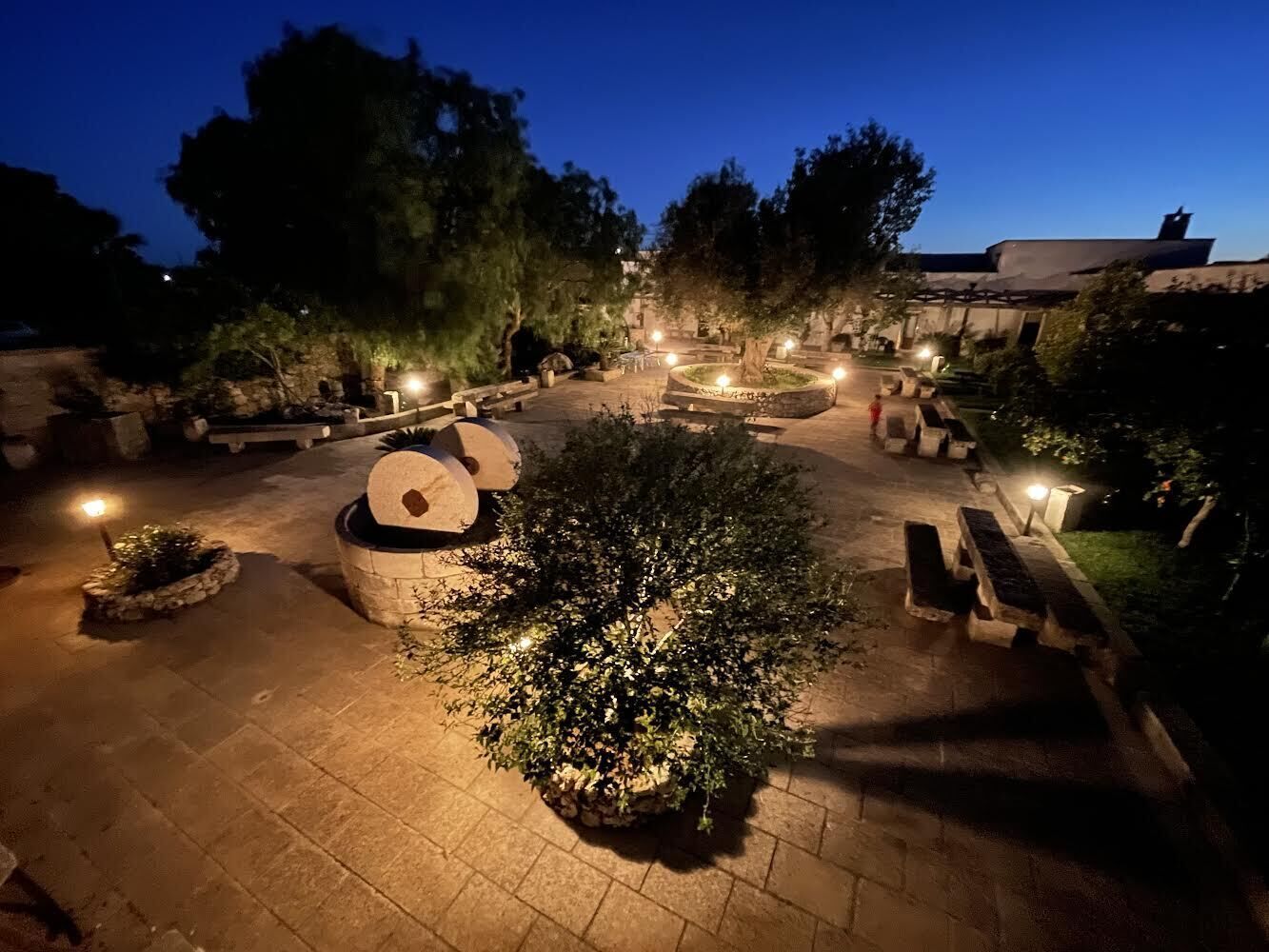 Un patio al aire libre con suelo de piedra, varios conjuntos de asientos e iluminación para plantas.