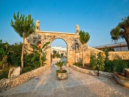 Un arco de piedra ornamentado con estatuas, rodeado de follaje y un camino empedrado.