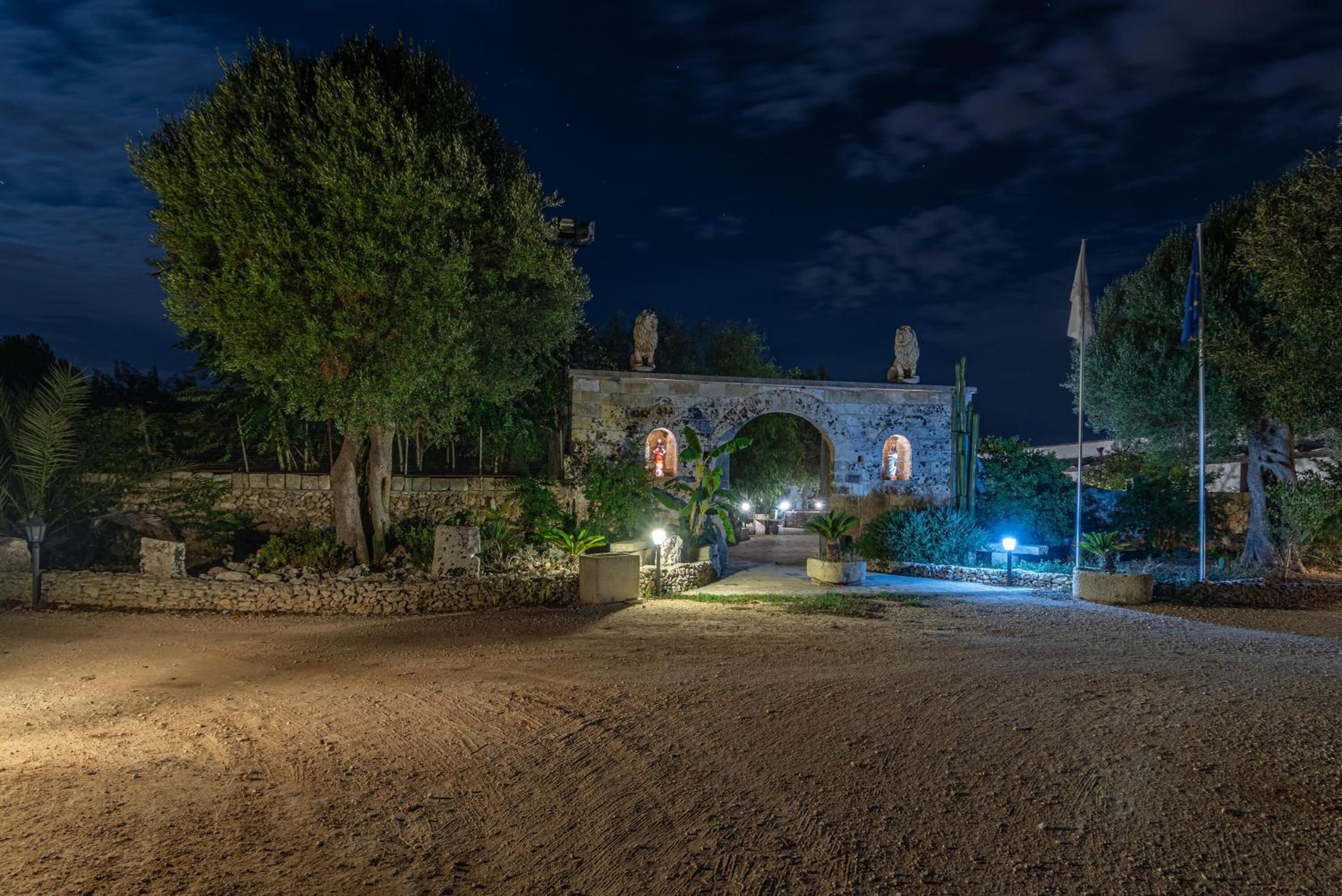 A nighttime view of a historic building with an arched entrance, surrounded by trees and illuminated by street lamps.