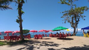 A beach with red and green umbrellas, plastic chairs, and a clear view of the sea.