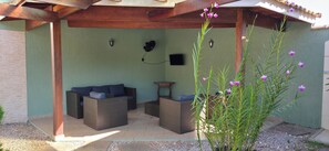 An outdoor seating area with wicker furniture, a pergola, and a wall-mounted TV.