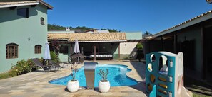 A swimming pool with lounge chairs, a children's play area, and a patio with a table and chairs.