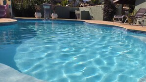 A clear swimming pool with lounge chairs and potted plants around it.