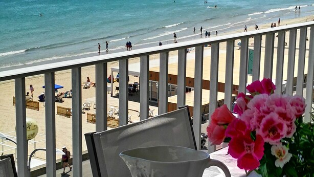 A table with a pitcher, a plate with fruit, and a vase with flowers, overlooking a beach with people and a clear blue sea. - Panoramic view  (La Baule-Escoublac)