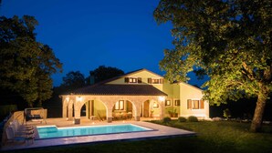 Ein zweistöckiges Haus mit Swimmingpool, steinernen Bogen und Sitzbereich im Freien.