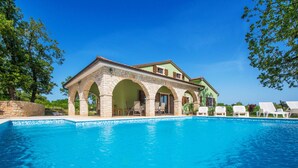 Ein Gebäude am Pool mit steinernen Bögen, einem Schwimmbecken und Liegestühlen.