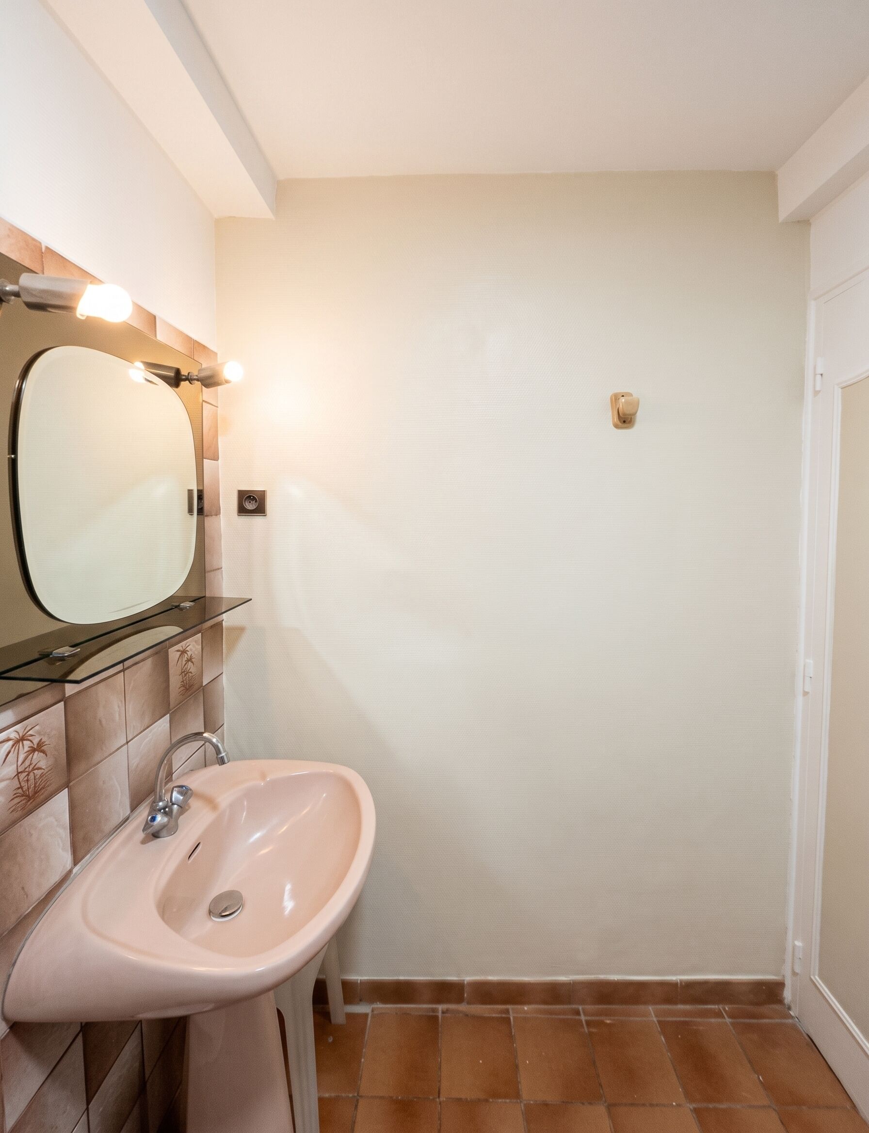 A bathroom with a sink, mirror, and wall-mounted light fixture.