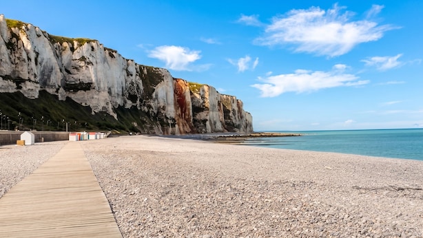 Ein Kiesstrand mit einer Holzpromenade, die zu einer Klippe führt.
