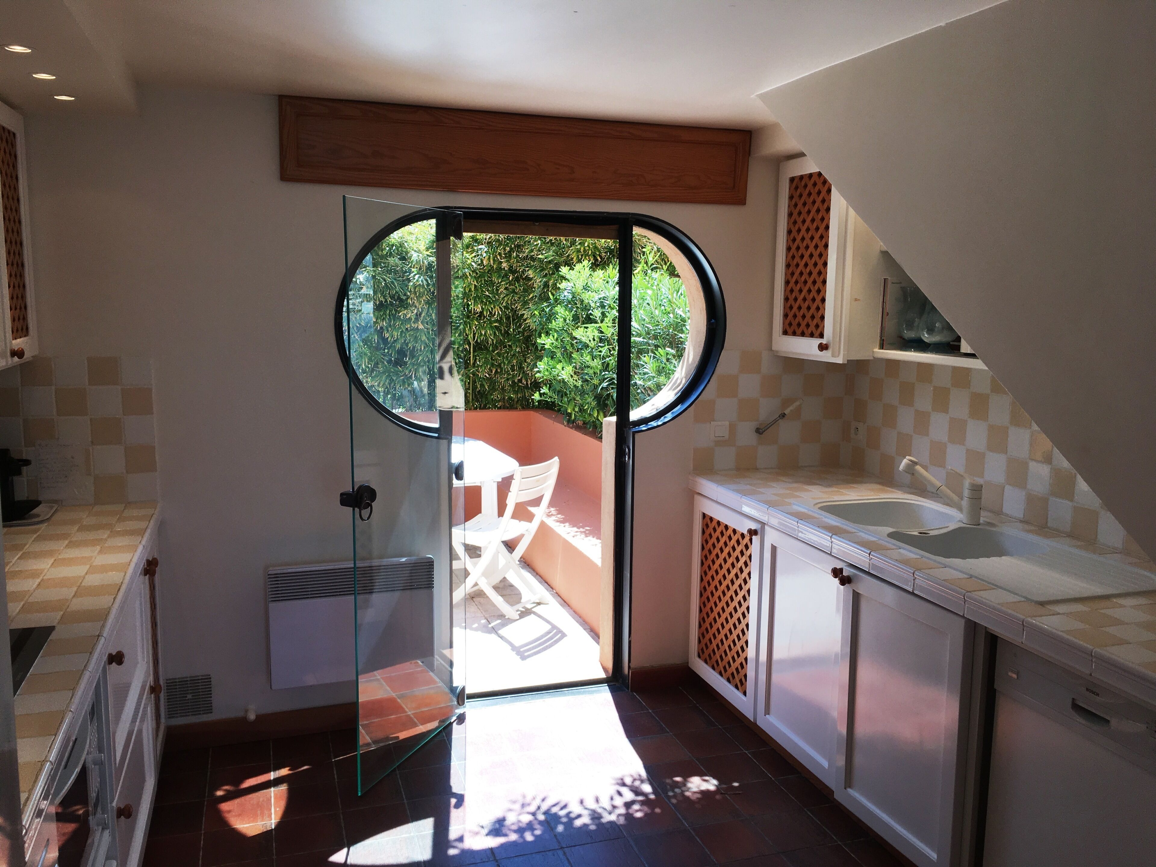 A modern kitchen with a glass door leading to an outdoor area, a sink, and a window overlooking greenery.