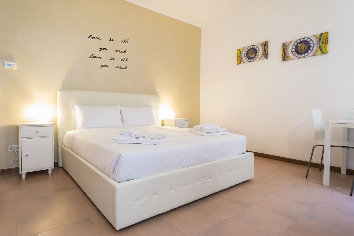 A neatly made bed with white linens and pillows, two bedside tables with lamps, and a wall with a motivational quote.