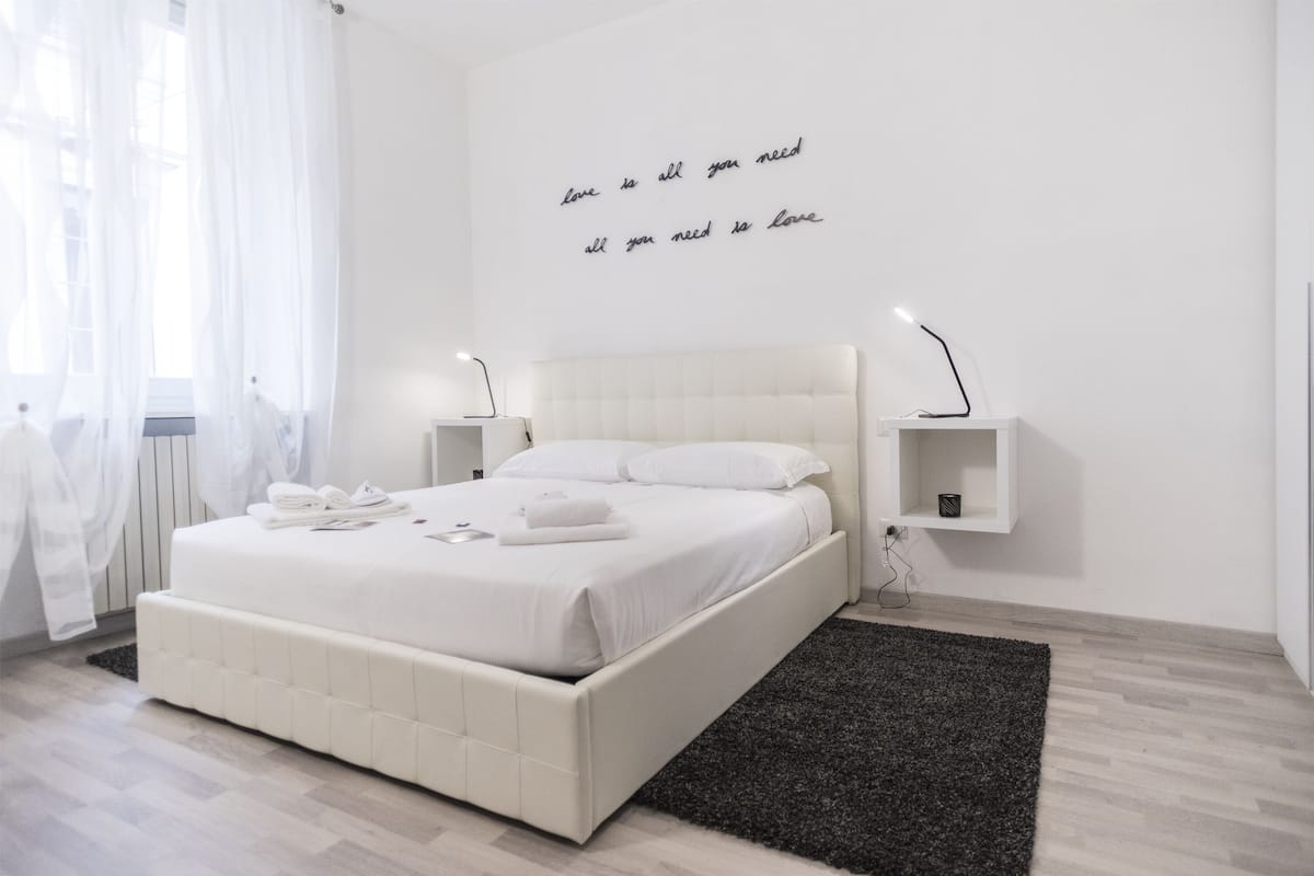A modern bedroom with a large bed, white bedding, a black rug, and a wall with a motivational quote.
