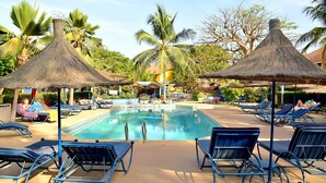 A pool area with lounge chairs and thatched umbrellas, surrounded by palm trees. - Villa Kadia Paradis 2 (Saly)