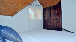 A bedroom with a bed, a window with curtains, and a wooden door. - Villa Kadia Paradis 2 (Saly)