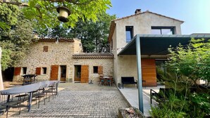 Un bâtiment en pierre doté d’une extension moderne, d’une terrasse extérieure et d’une cour pavée.