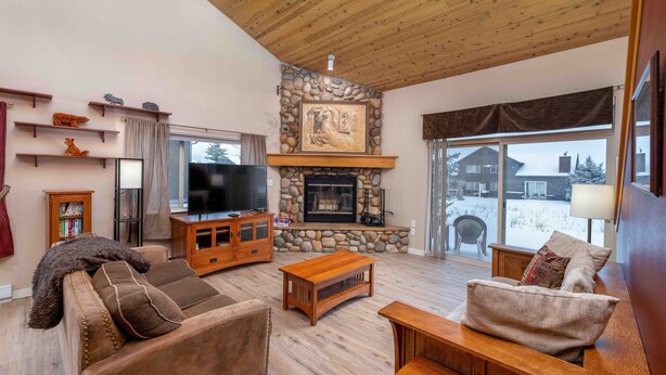A cozy living room with a stone fireplace, wooden furniture, and a television.