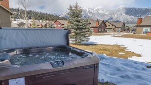 A hot tub with a view of snow-covered mountains and houses in the background.
