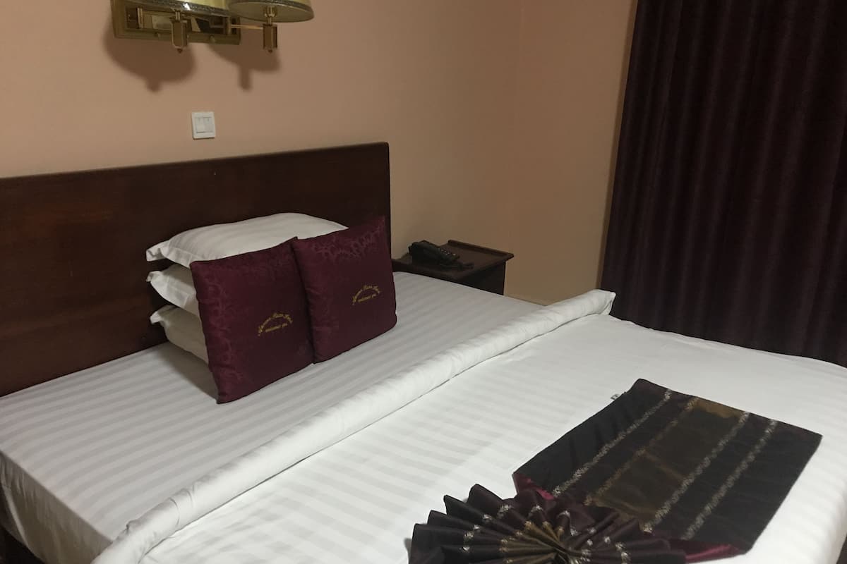 A hotel room with a neatly made bed, a bedside table with a phone, and a wall-mounted lamp.