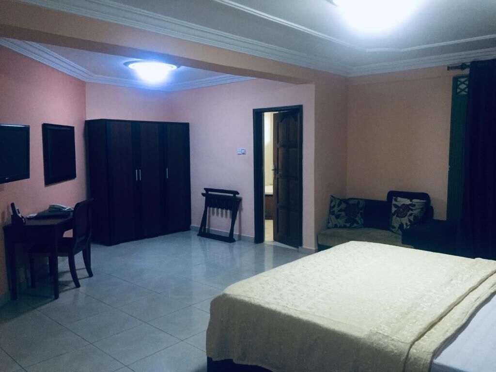 A bedroom with a bed, a desk, and a chair. There is a wardrobe and a television on the wall.