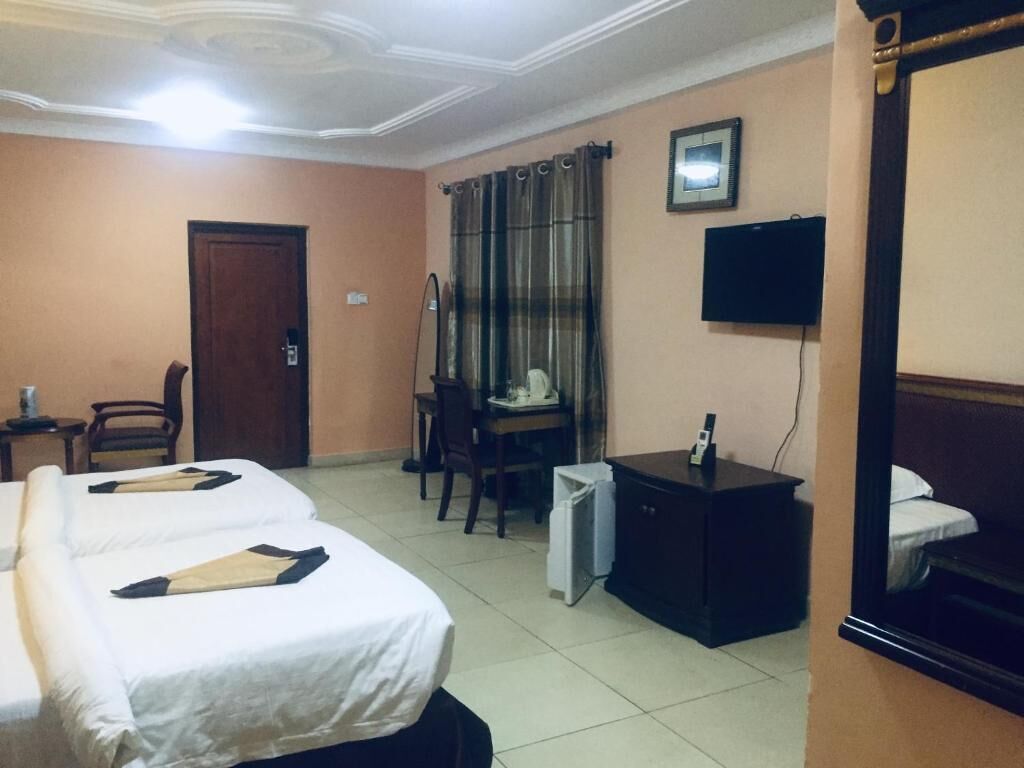 Una camera d'albergo con due letti, una scrivania, una sedia, una televisione e un armadio.