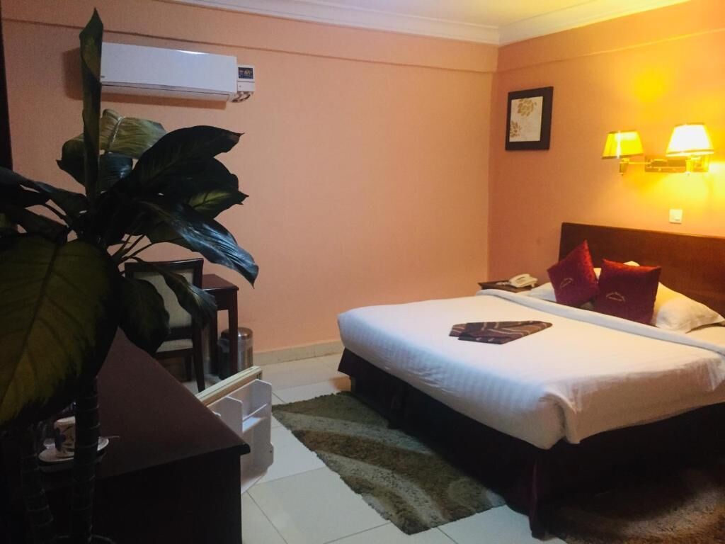 Une chambre d’hôtel avec un lit, des lampes de chevet, un bureau, une chaise et une plante en pot.