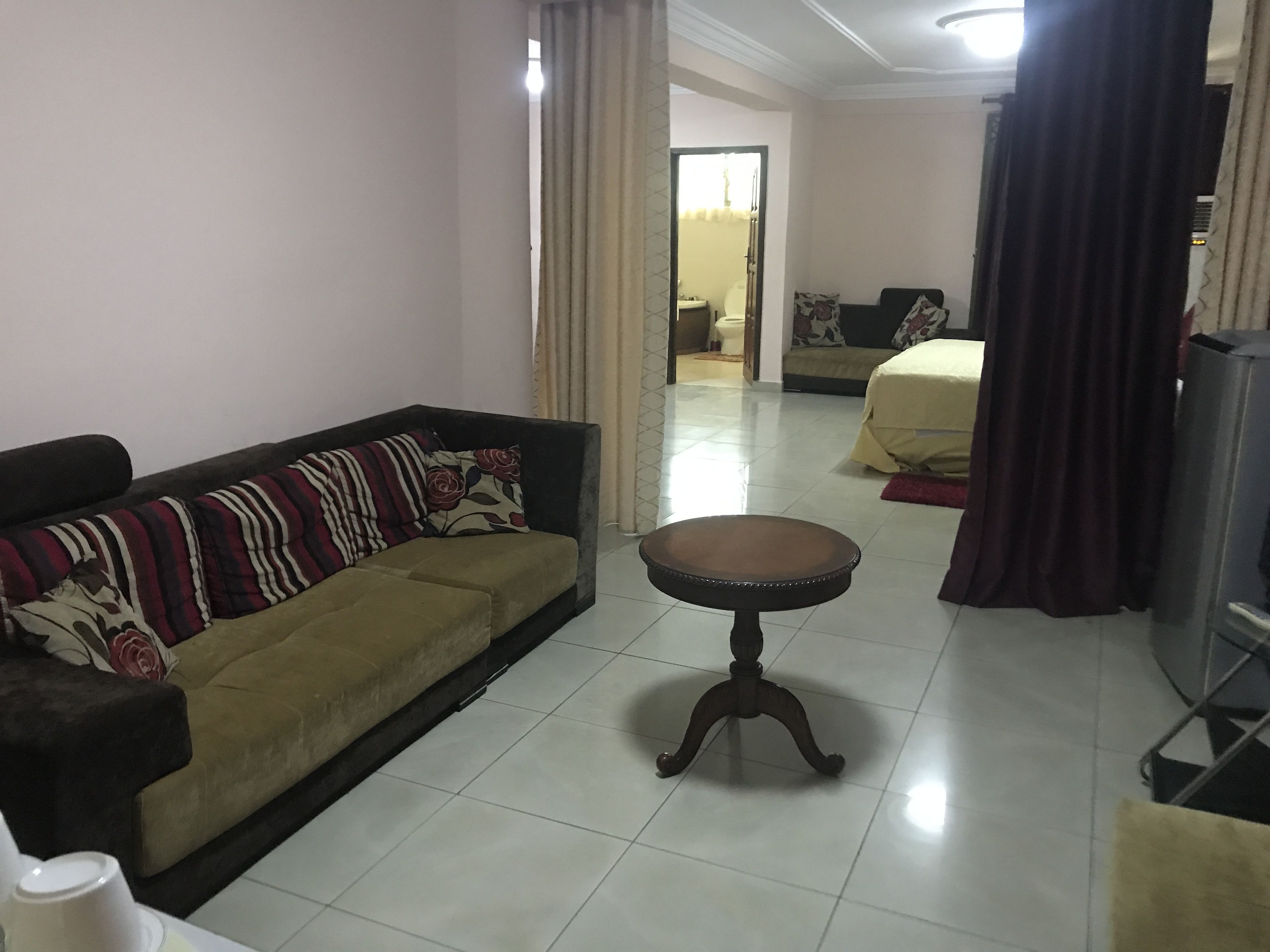 A living room with a sofa, a small round table, and a bed in the background.