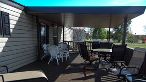 Een overdekt terras buiten met rieten meubels, een tafel en een barbecue.