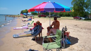 Een strandscène met mensen die ontspannen onder kleurrijke parasols, strandstoelen en op luchtbedden.