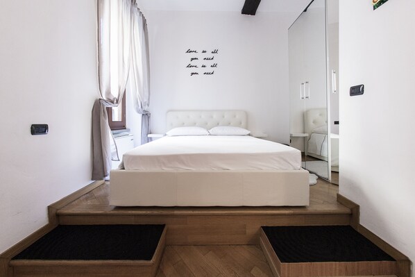 A bedroom with a bed, a bedside table, a mirror, and a wall with a motivational quote.