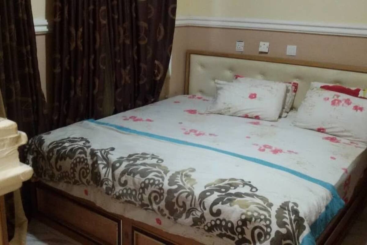 Uma cama com roupa de cama florida, uma cabeceira e uma mesa de cabeceira com abajur.