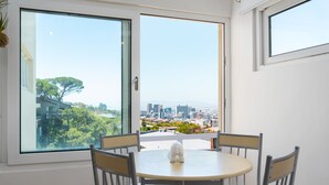 A dining area with a round table and four chairs, large windows offering a city view, and a small decorative elephant figurine on the table. - Harbour Lights 306 - Adults Only (Cape Town)