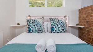 A neatly made bed with patterned pillows, a teal throw blanket, and rolled towels on the bed. - Harbour Lights 306 - Adults Only (Cape Town)