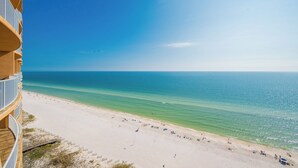 Uitzicht op het strand vanaf een balkon, met een heldere lucht en rustige zee.