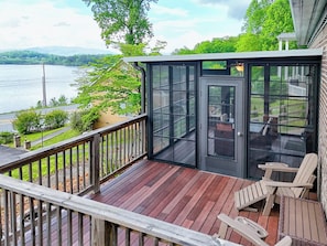 A wooden deck with a glass door leading to a patio area with outdoor furniture. - Lake Chatuge Bungalow by Chatuge Home Concierge | Cozy Pet-Friendly Retreat · Lake & Mountain Views · Firepit (Hiawassee)