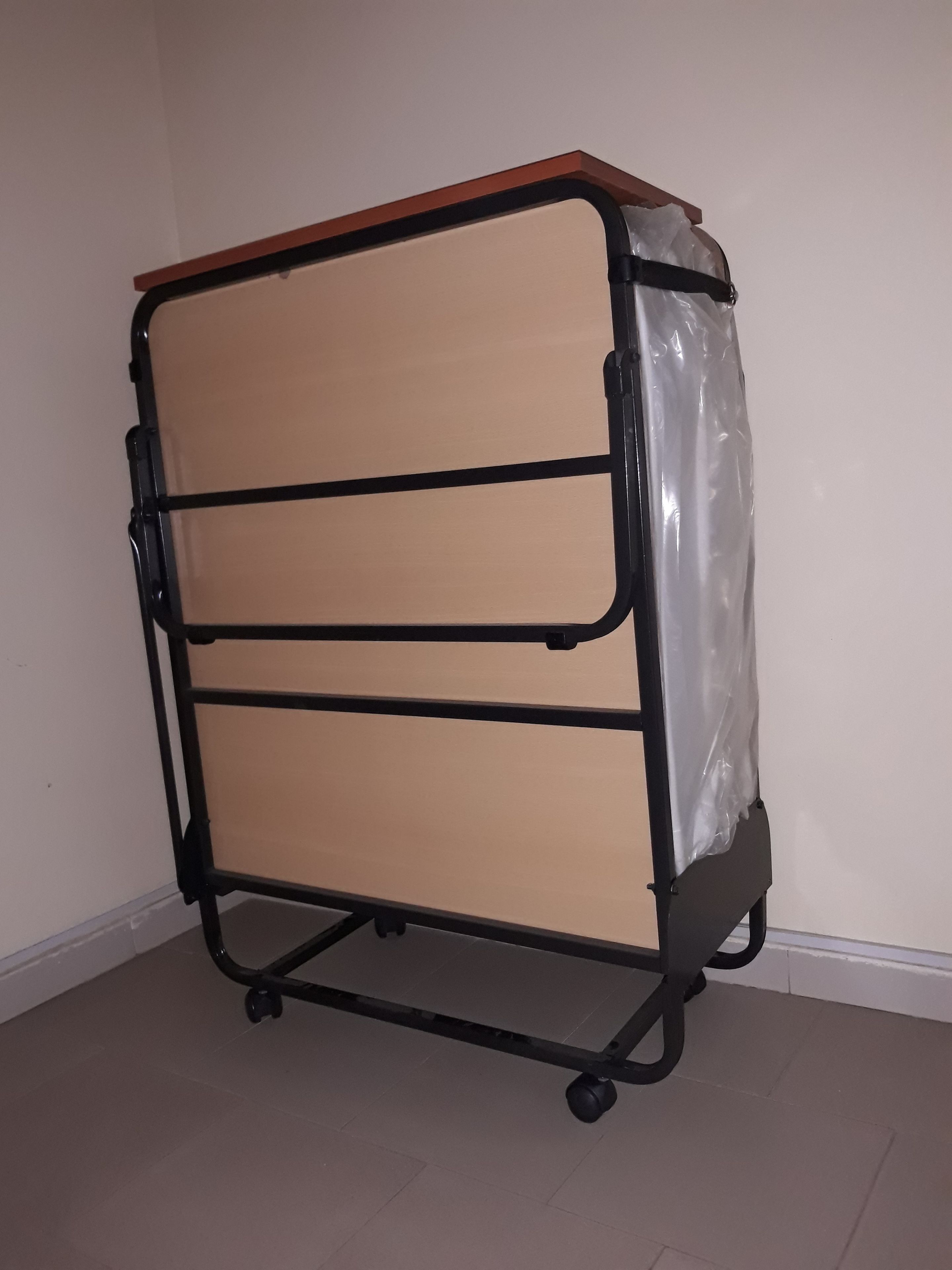 A black metal storage cart with three beige drawers, positioned against a plain wall with a tiled floor.