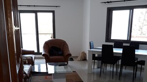 Un vaste espace de vie doté d’une grande fenêtre, d’un fauteuil en cuir marron, d’une table basse en verre et d’un coin repas avec des chaises noires.