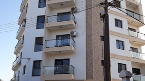 Un immeuble résidentiel à plusieurs étages, doté de balcons, de climatiseurs et d’une entrée sécurisée par un portail.