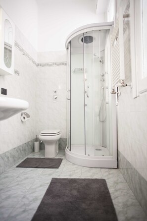 Ein modernes Badezimmer mit einer gläsernen Duschkabine, einem weißen Waschbecken und einer Toilette.