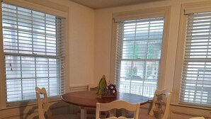 Un área de comedor con una mesa redonda y cuatro sillas, una mariposa decorativa sobre la mesa y un sofá beige al frente.